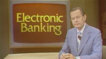 1970s television still: a presenter in a suit in front of a large sign reading Electronic Banking