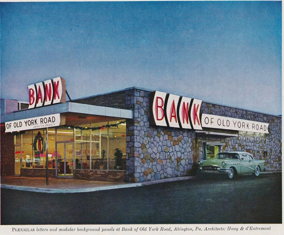 1950s colour photograph of the Bank of Old York Road in Abington, Pennsylvania, at dusk, with large Plexiglas BANK letters on a stone facade and a green car at the drive-through